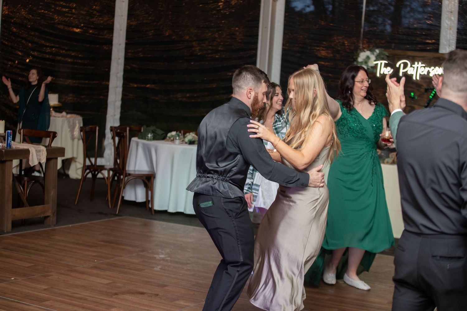 Couple dancing together at a wedding reception in a tent venue with guests watching in background.
