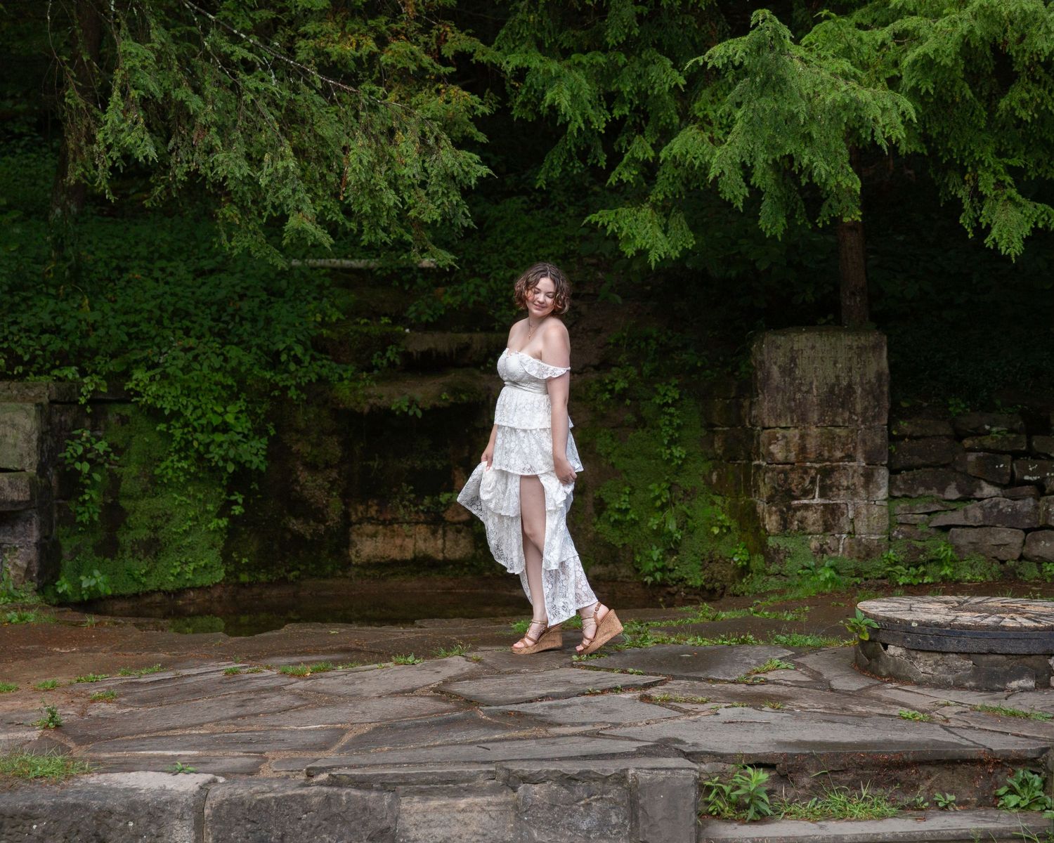 Person in white dress walking along stone pathway in green garden setting.