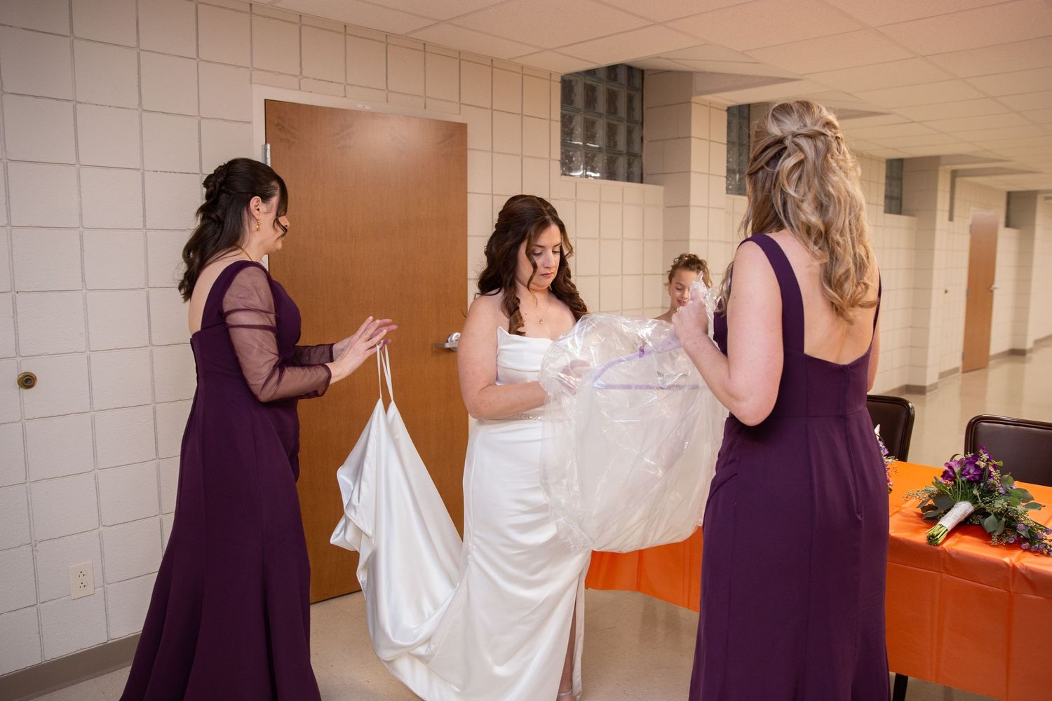 Wedding party members in purple and white dresses walking down a hallway.