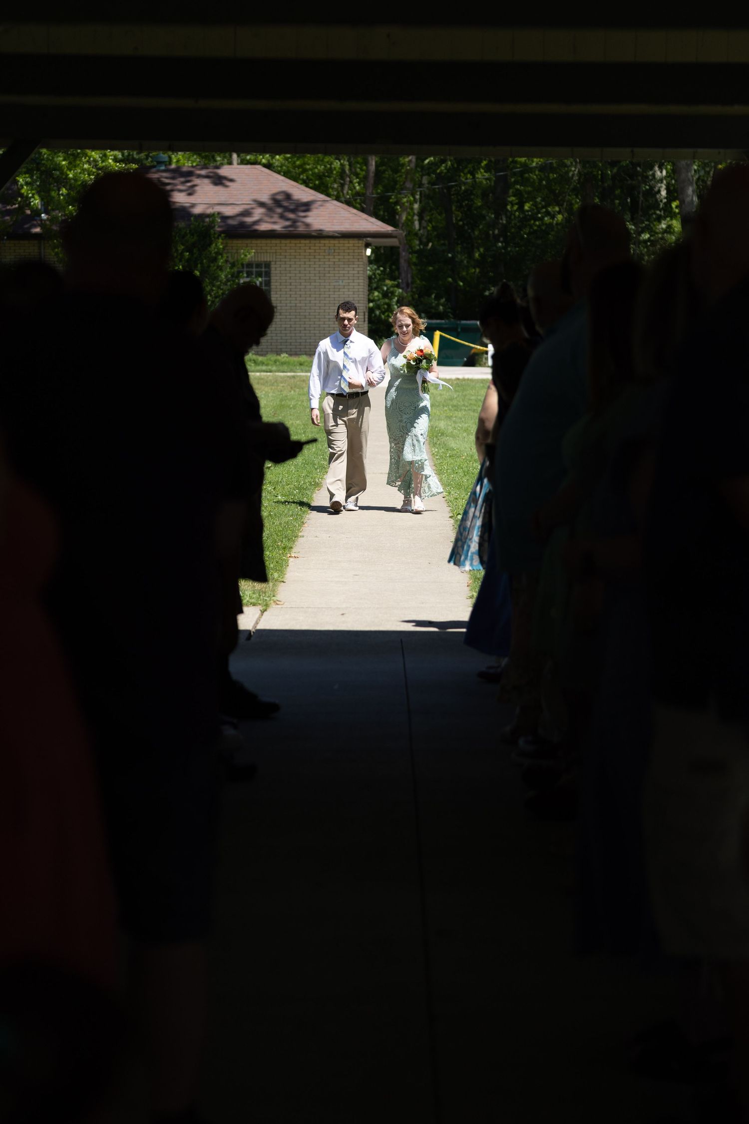 Wedding processional viewed through a dark doorway frame.