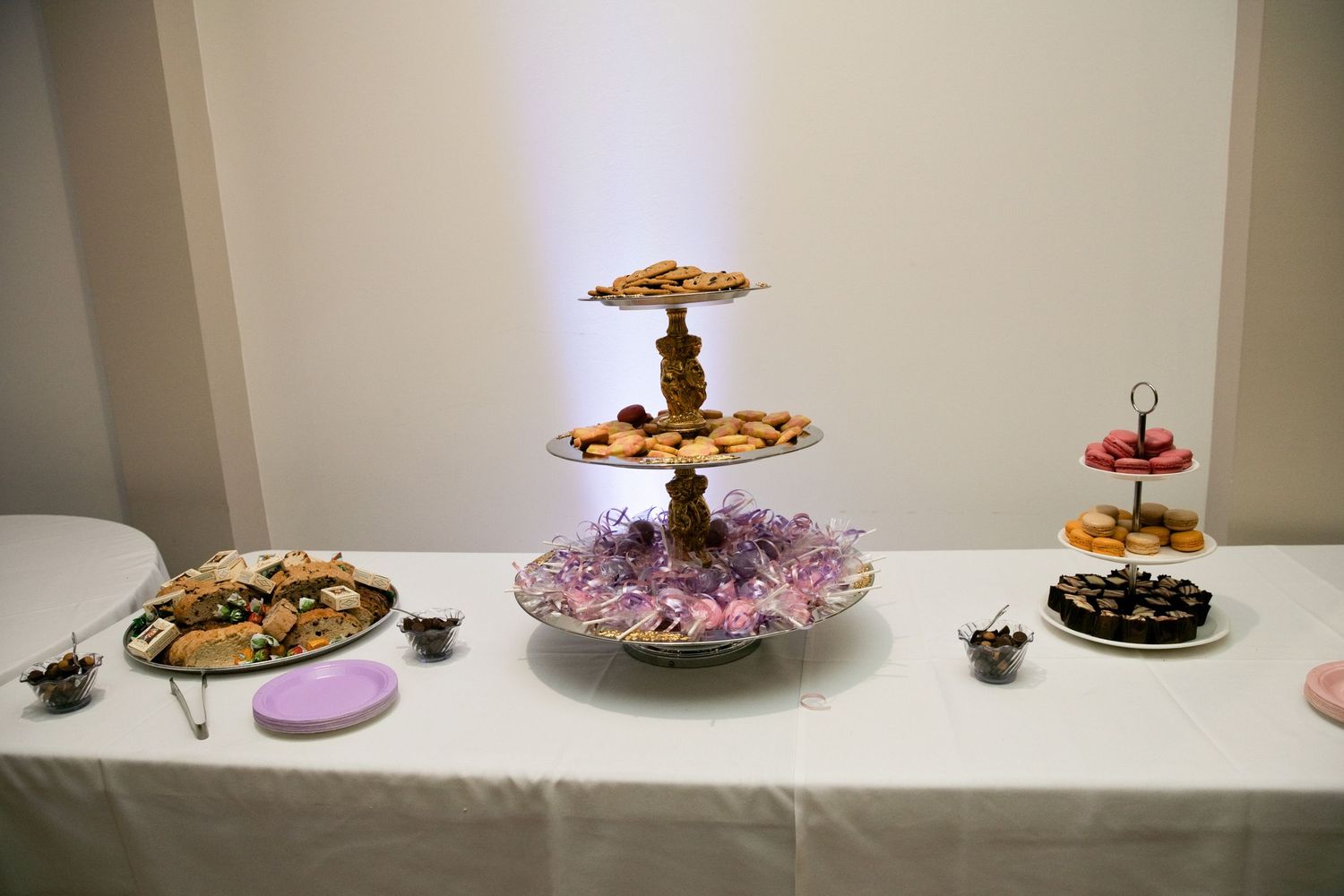 Elegant wedding dessert table with tiered cookie stand, assorted pastries, and donuts on white tablecloth.