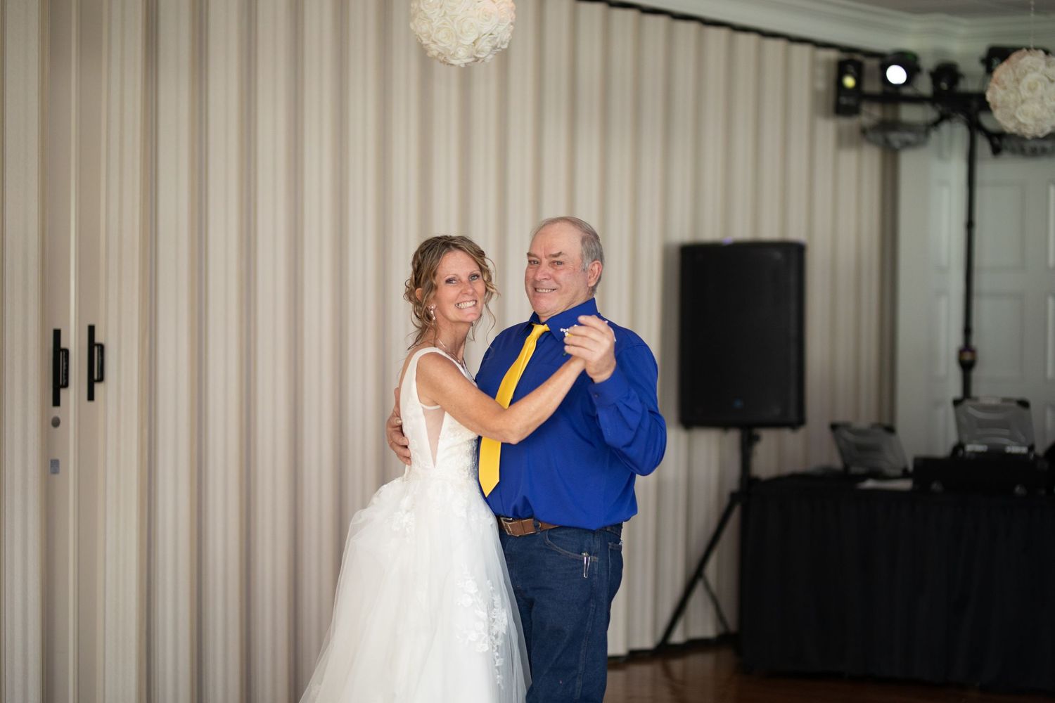 Bride and older man share a father-daughter dance at a wedding reception in a decorated ballroom.