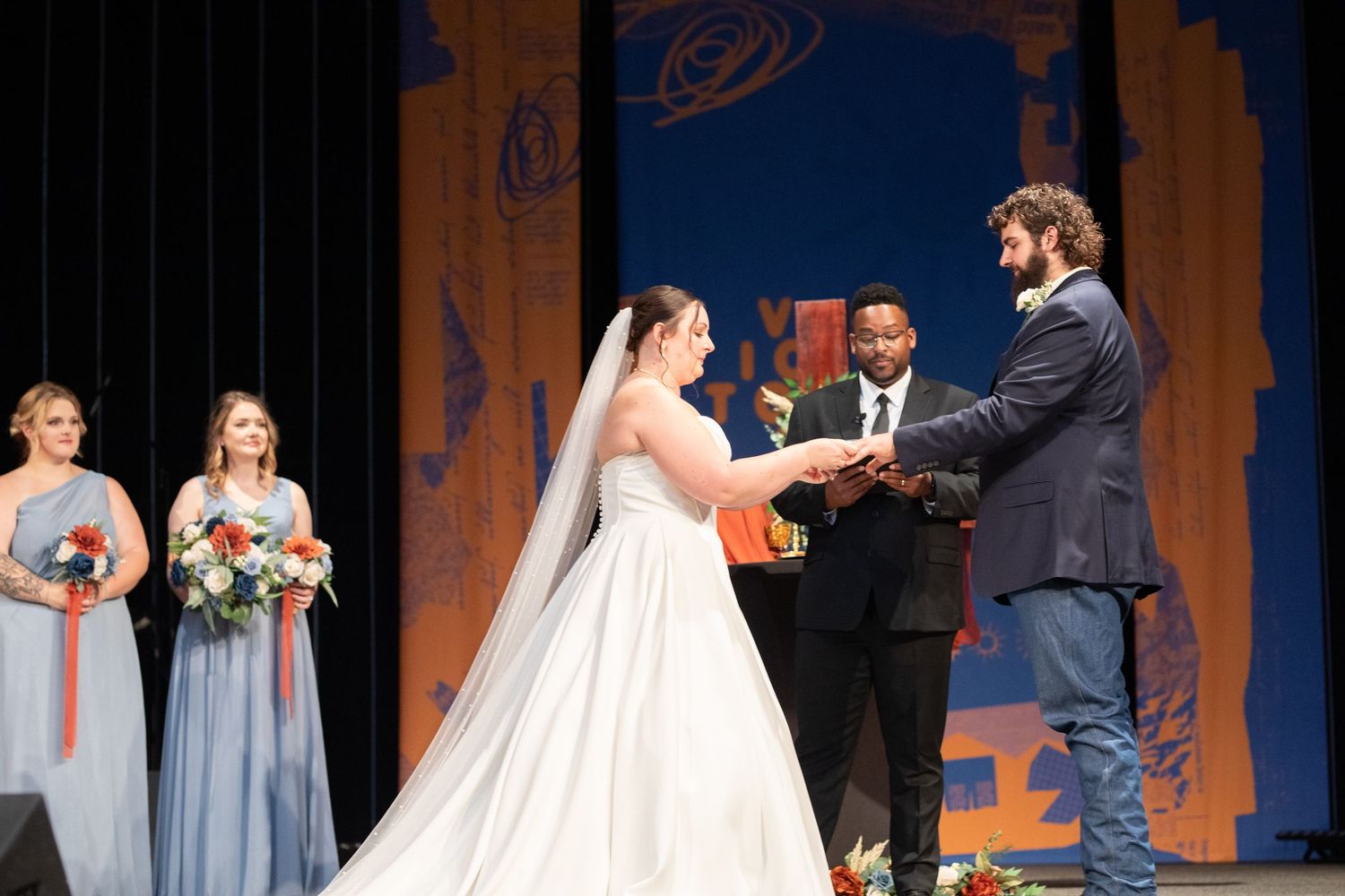 Wedding ceremony with bridal party in gray and coral dresses watching the vow exchange.