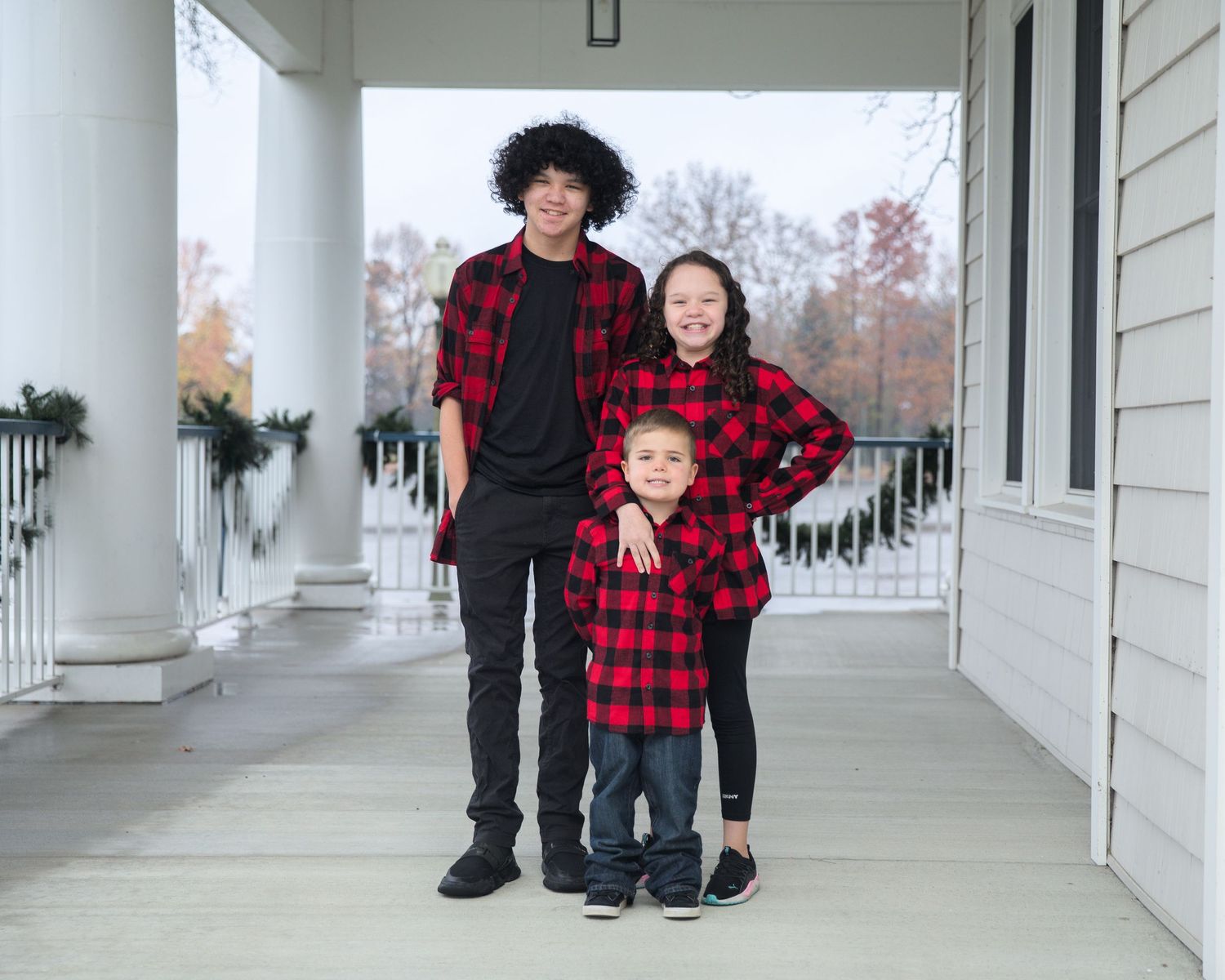 A group poses on a white columned porch wearing coordinated holiday outfits.