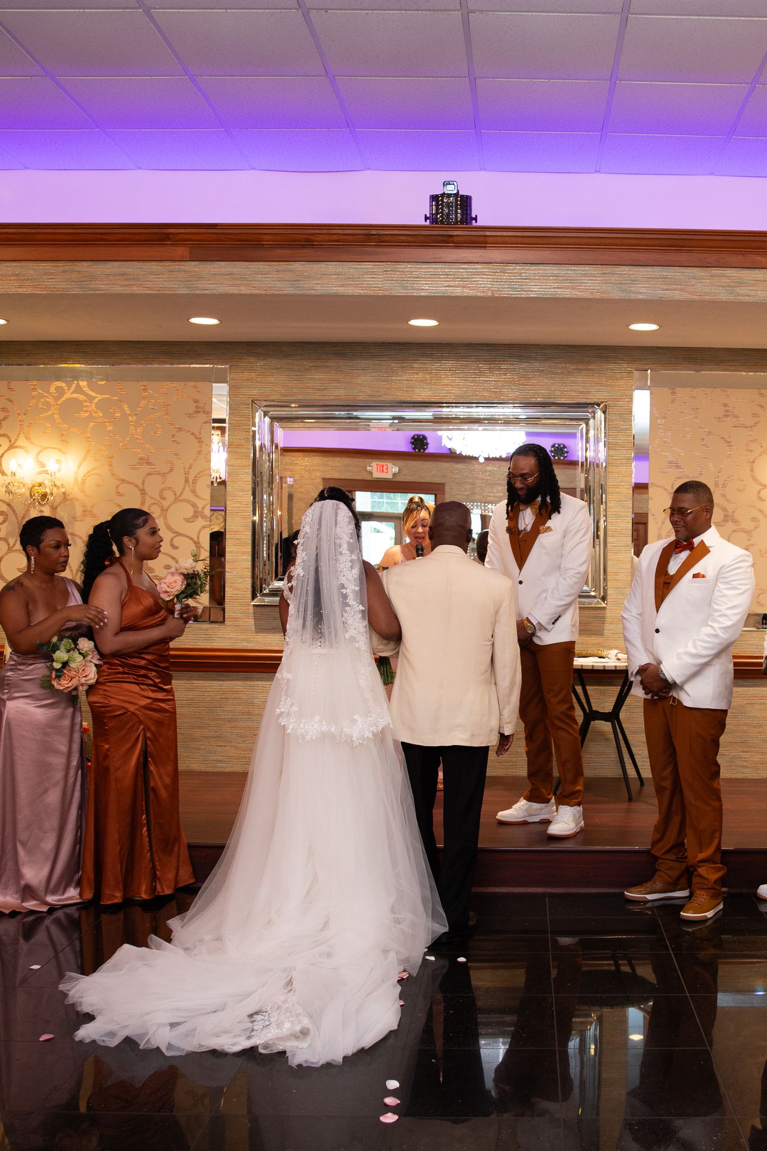 Wedding party lines up in formal attire with white and brown color scheme in reception hall.