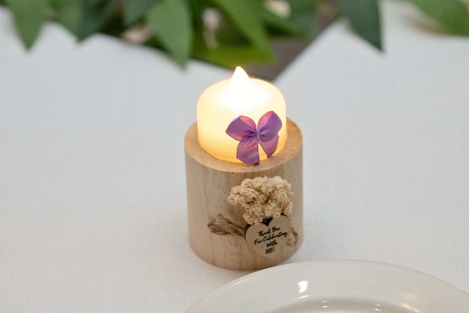 Small wooden tealight candle holder with a glowing LED candle, decorated with a purple flower and dried botanicals.