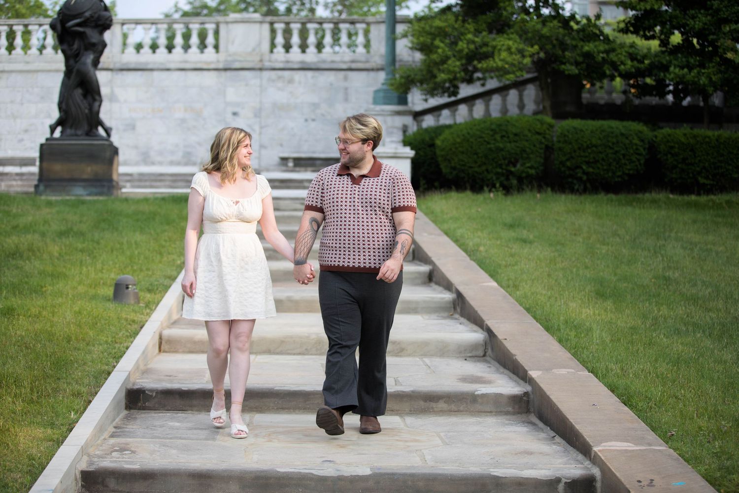 Couple walking together along a white stone balustrade in a garden setting.