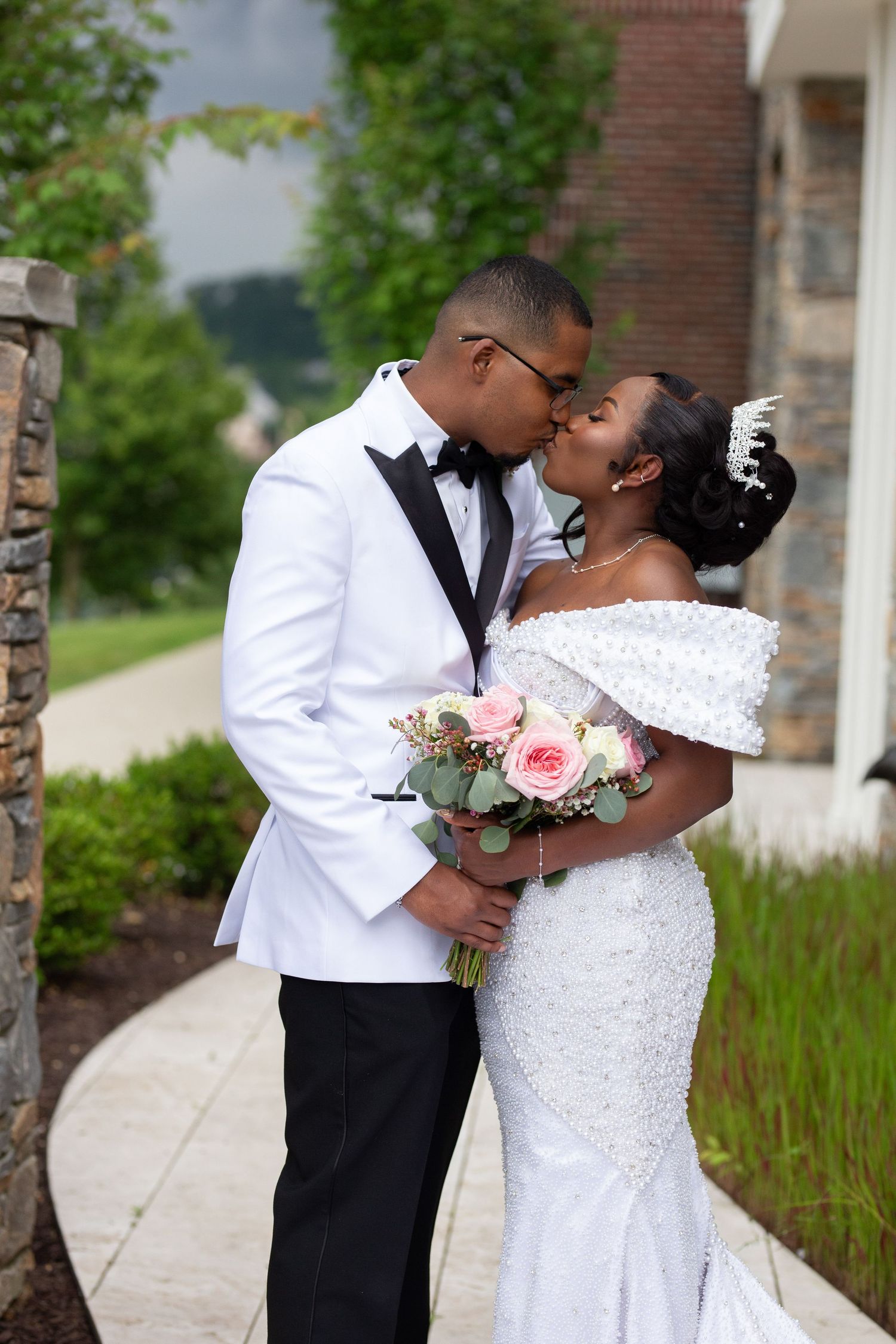 Romantic wedding couple posing outdoors against stone pillars and greenery.