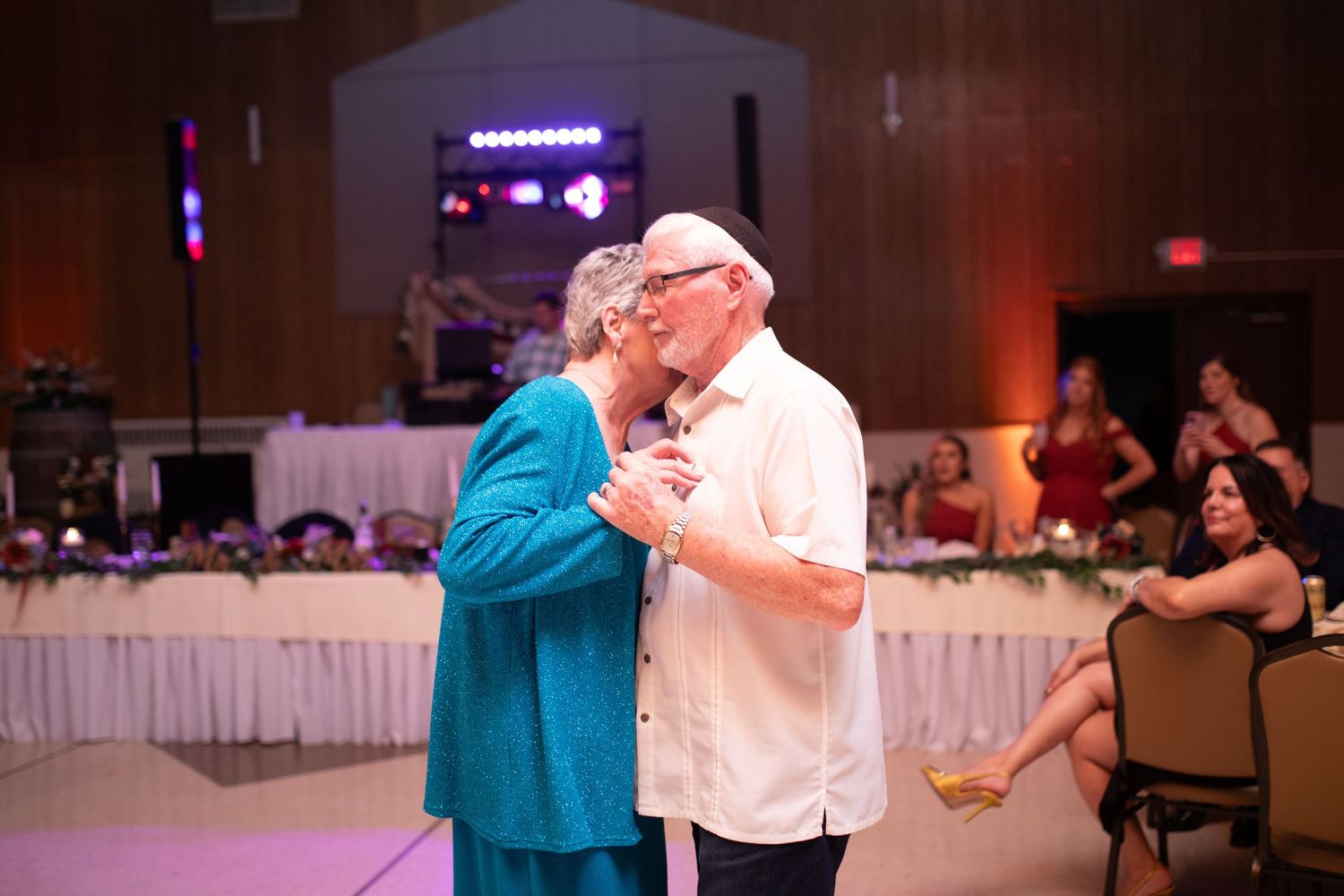 Wedding reception guests dancing in formal attire under dimmed lighting.