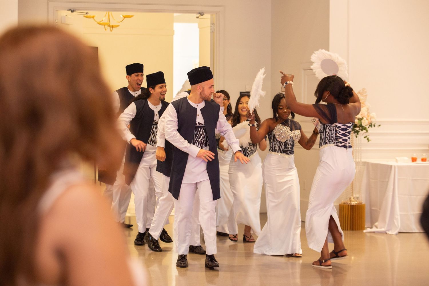 Wedding party dancing and celebrating in formal attire at an elegant white reception venue.