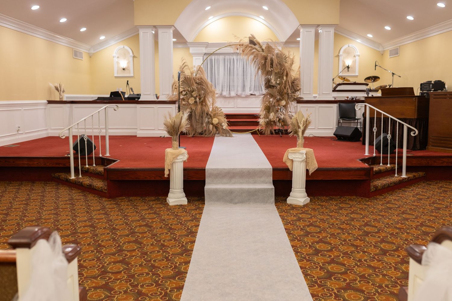 Wedding ceremony venue with white aisle runner, floral arch, and red carpeted stage.