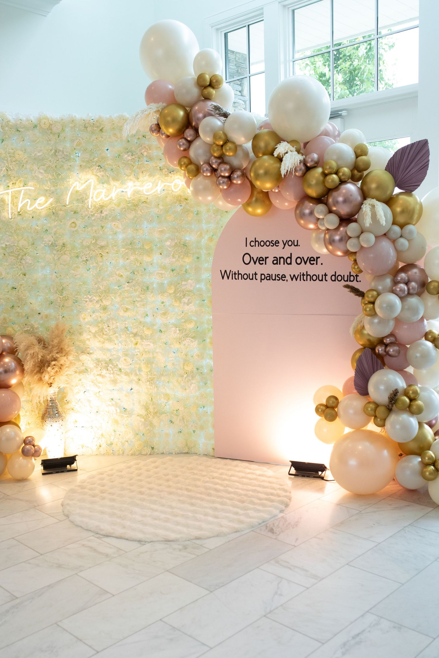 Modern event space with balloon arch installation and neon sign against floral wall.