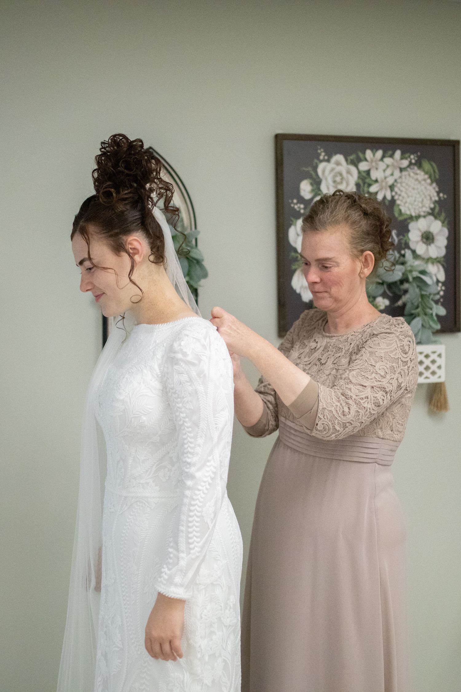 Final adjustments being made to a wedding dress and veil in a room with floral wall art.