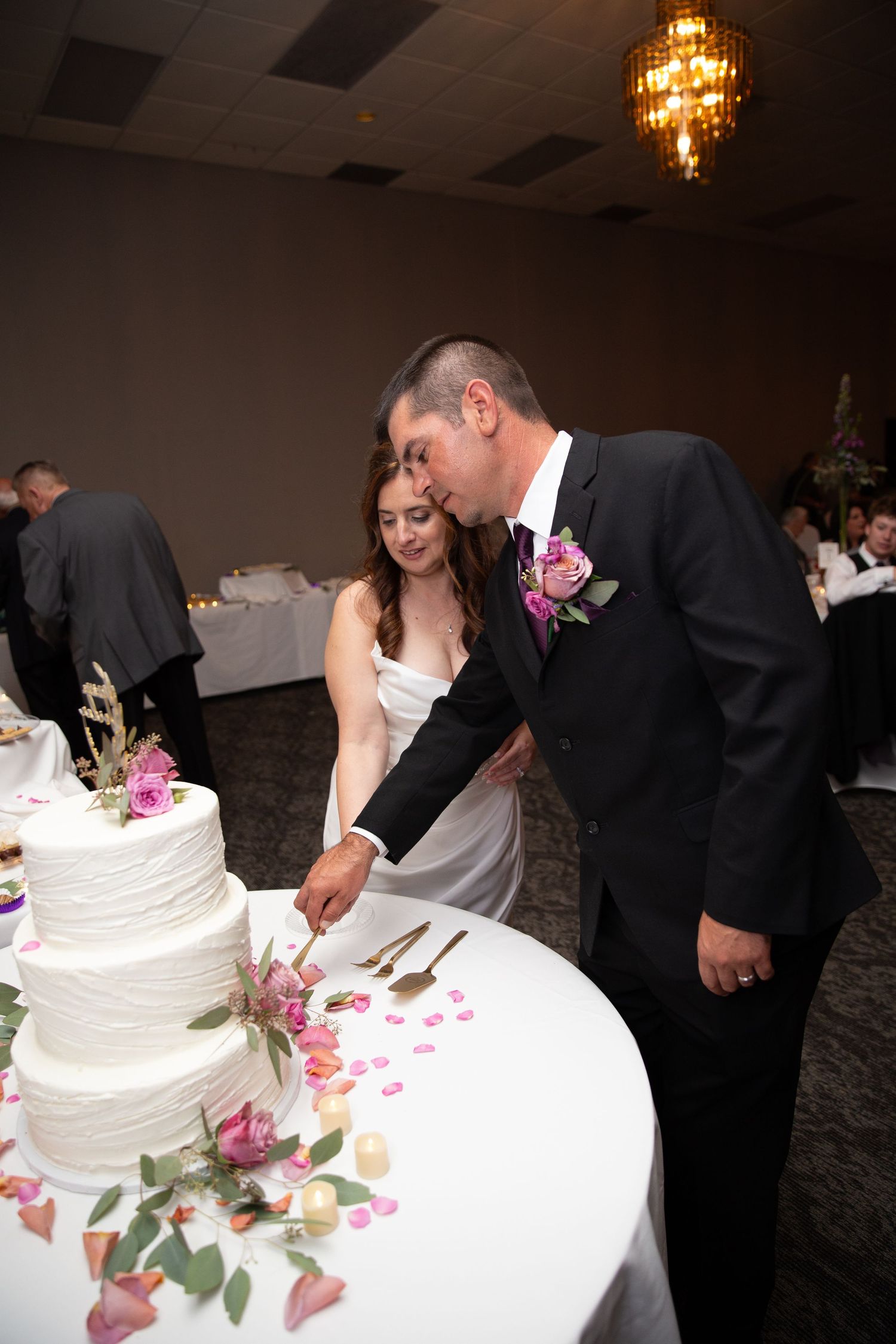 Wedding cake cutting ceremony with a multi-tiered white cake decorated with pink flowers.
