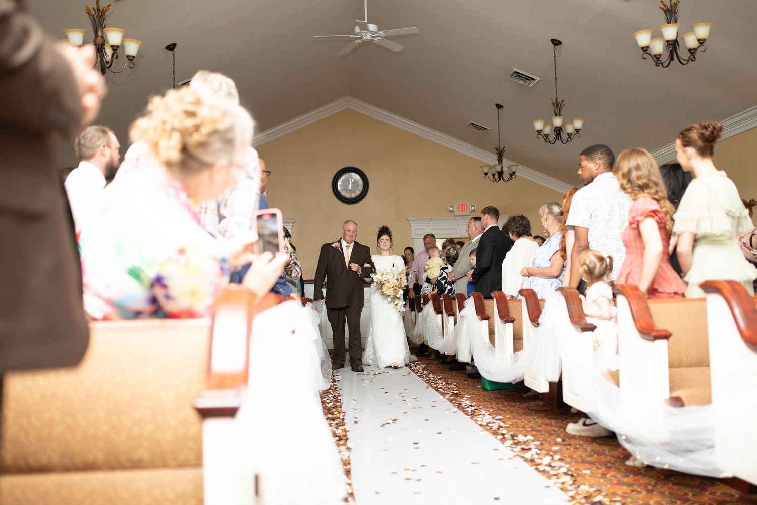 Wedding ceremony procession in an elegant venue with white decor and red carpet aisle.