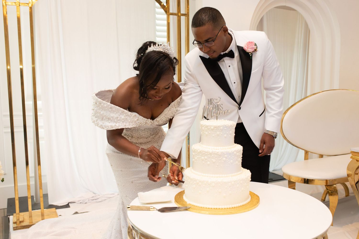 Newlyweds sharing intimate moment while cutting their elegant white wedding cake.