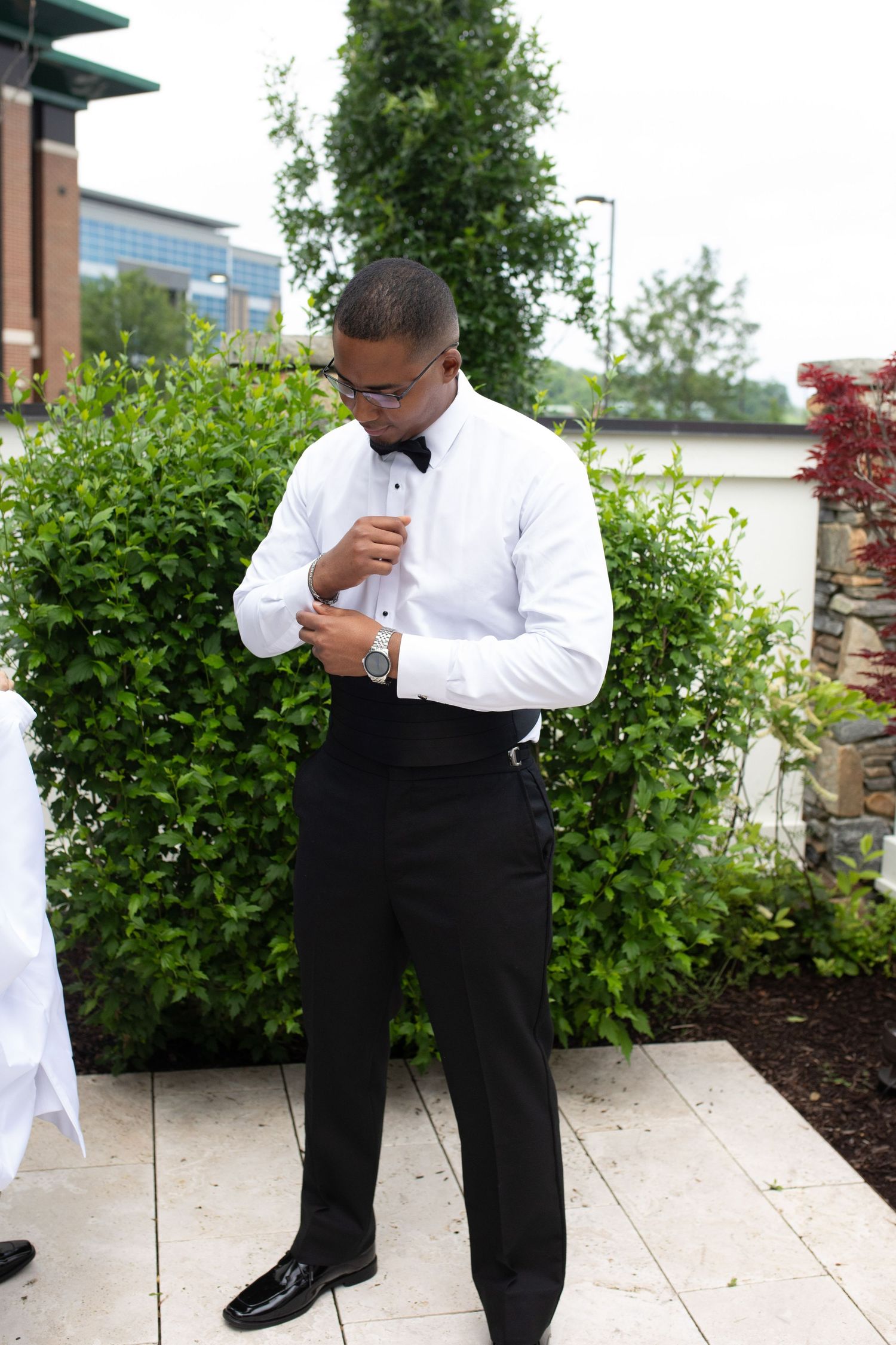 Groomsmen in formal attire perform a playful photo sequence outdoors near greenery.