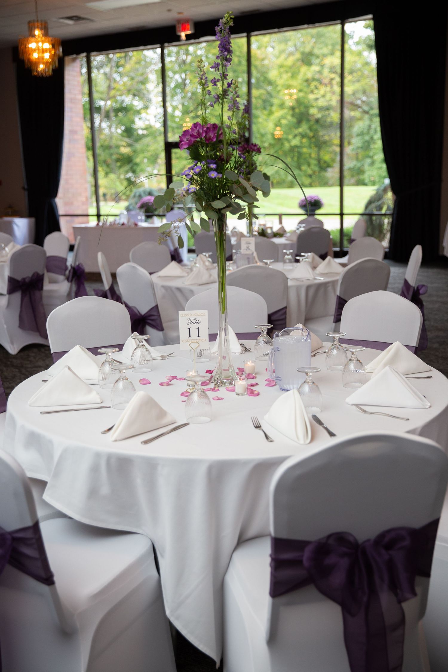 Wedding reception tables decorated with white linens, purple chair sashes, and elegant floral centerpieces.