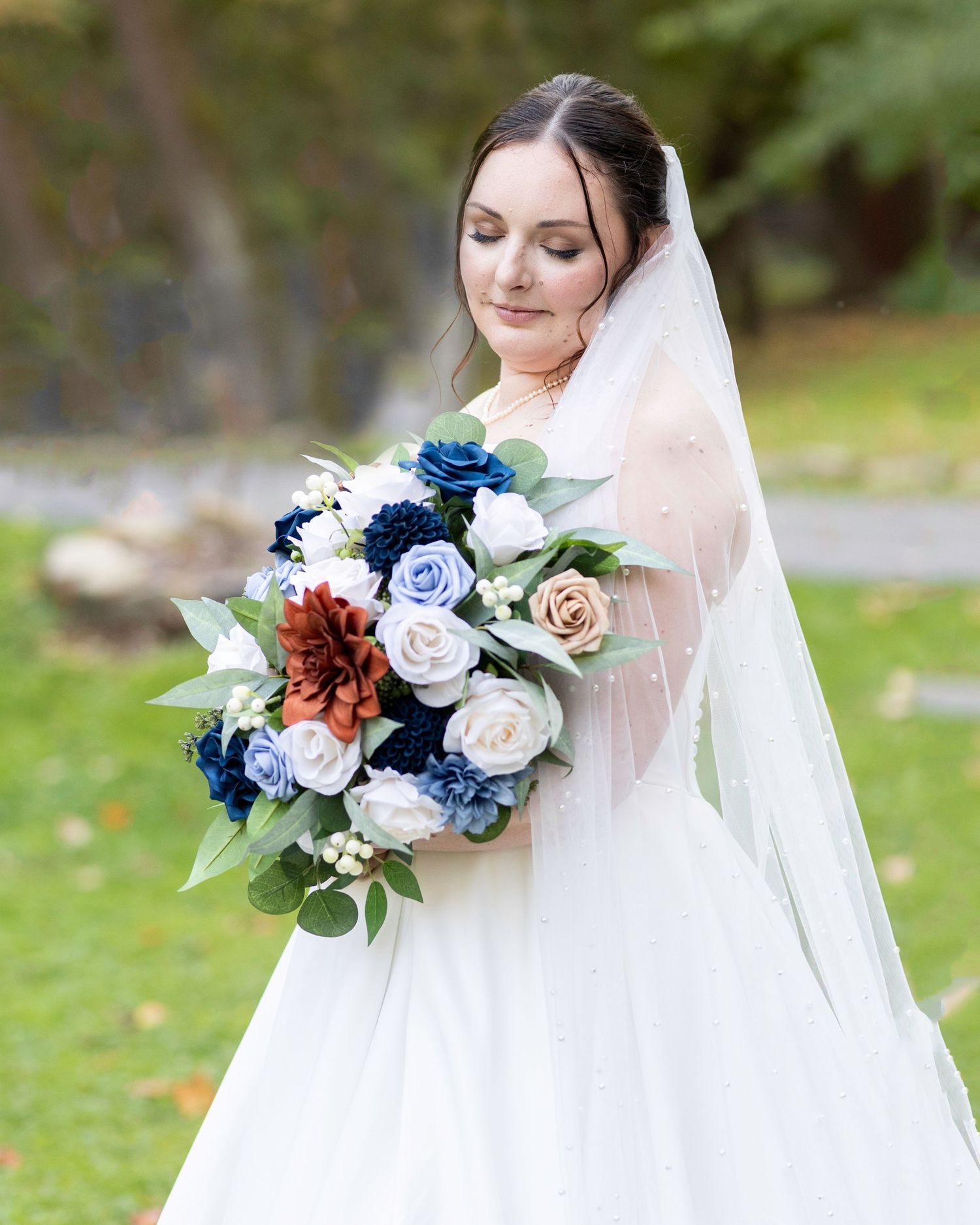 A bride holds an elegant bouquet with blue roses and burgundy flowers against her white wedding dress.