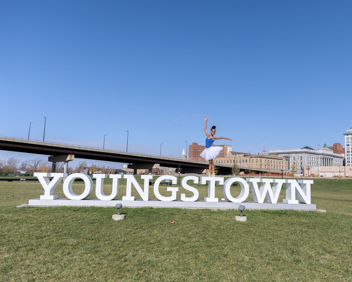 Someone jumps playfully in front of large white Youngstown letters on grass.