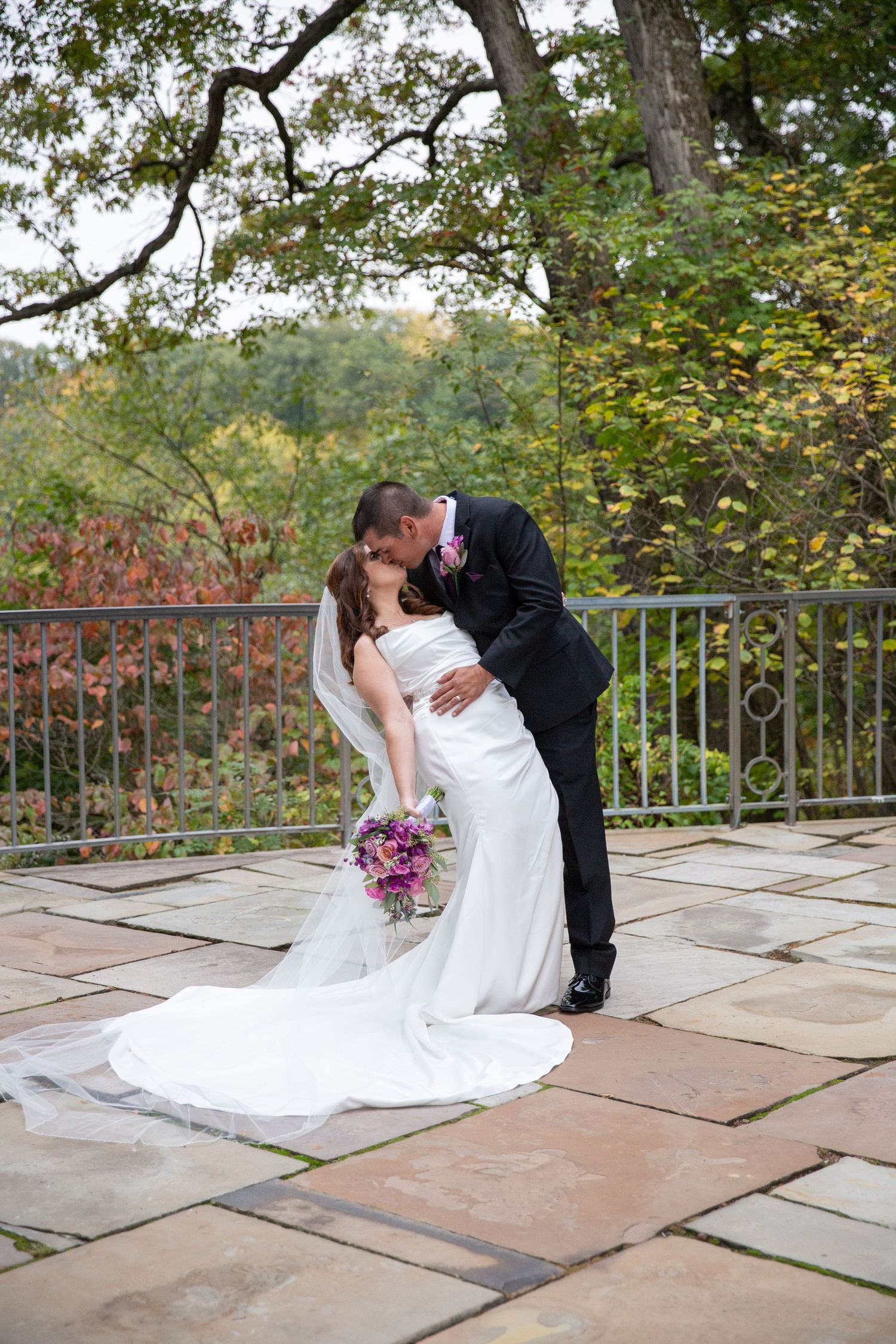 Romantic wedding portraits on stone patio with flowing white dress and autumn foliage.