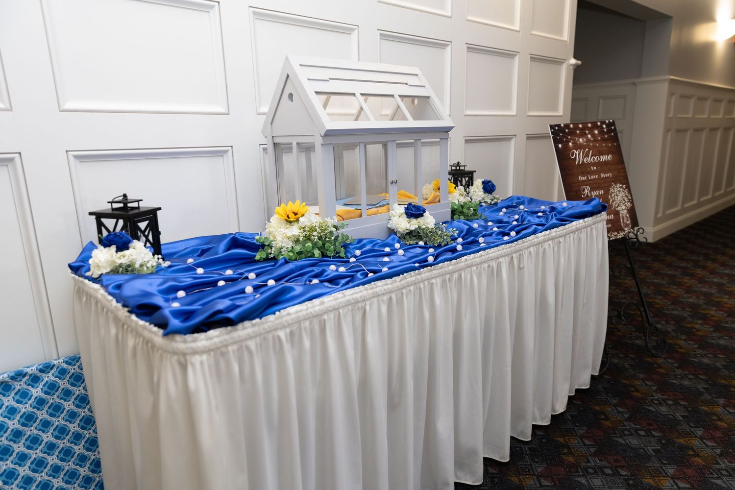 Elegant wedding reception table with royal blue satin draping, white floral arrangements, and a decorative card box centerpiece.