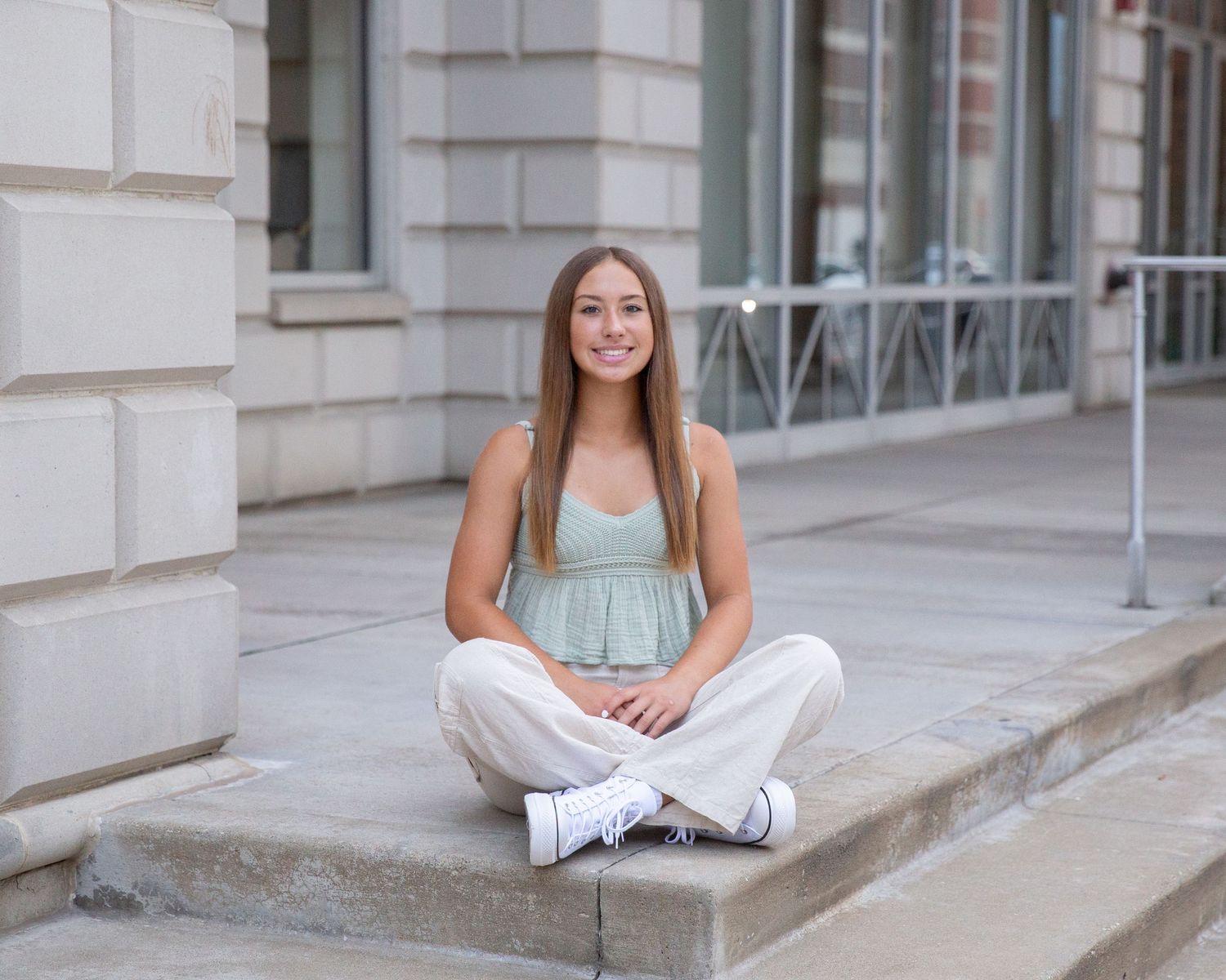 A person in casual attire sits cross-legged on concrete steps near a building.