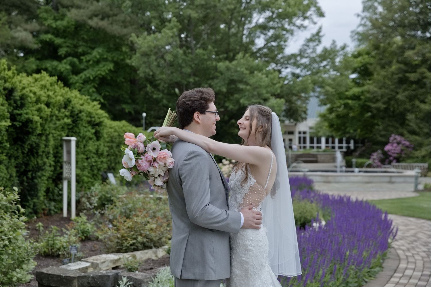 Bride and groom share a tender moment in a lush garden, surrounded by lavender blooms and greenery on their wedding day.