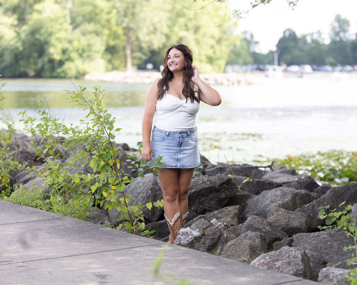 Casual summer outfit with cowboy boots posed along a rocky waterfront path.