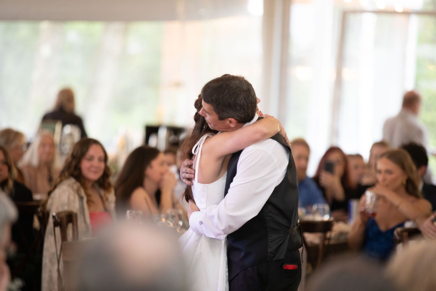 Bride and groom share an emotional first dance embrace at their wedding reception with guests watching.
