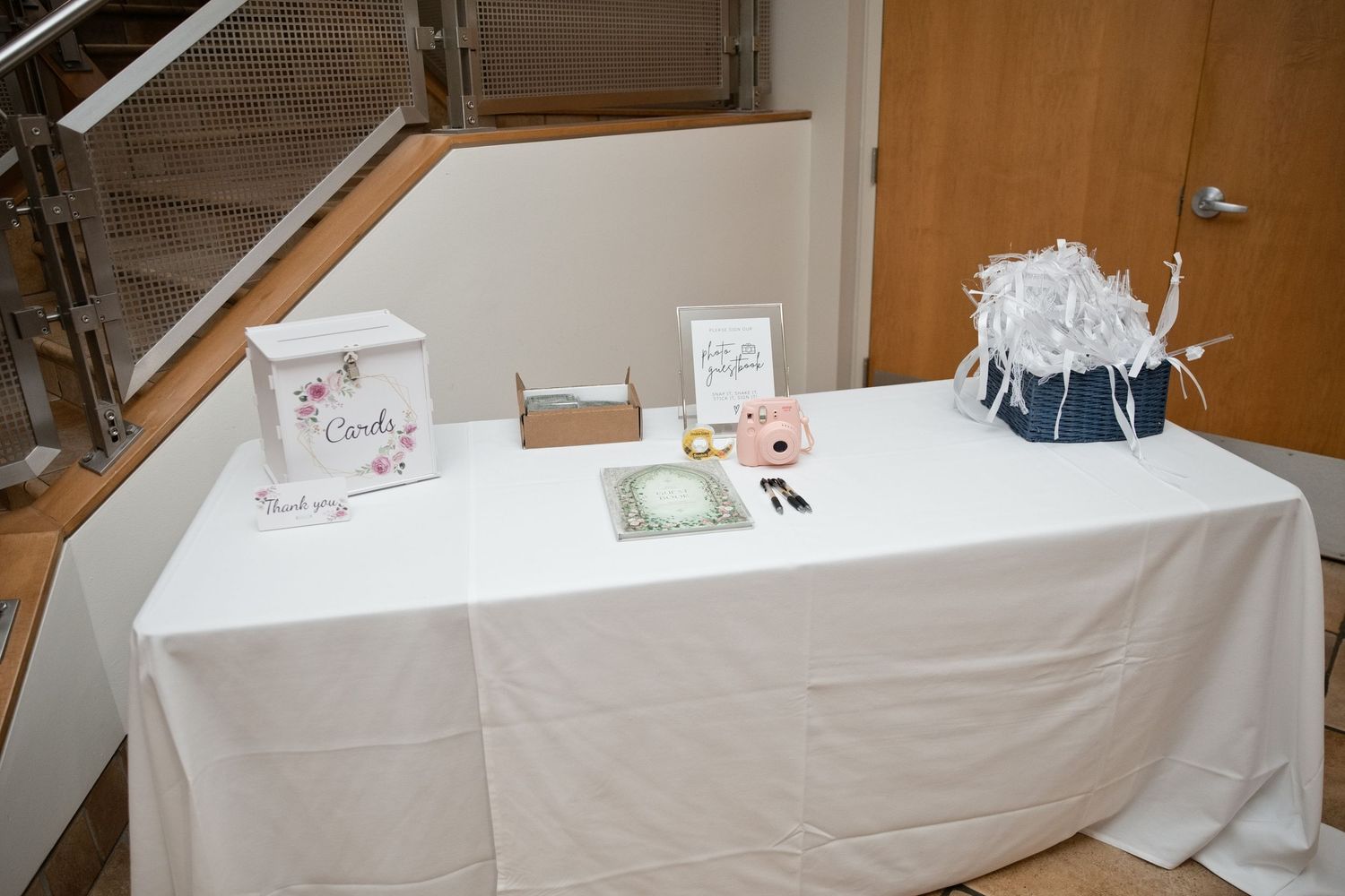 Elegant wedding guest book table with white tablecloth, card box, floral bouquet, and decorative items at a reception venue.