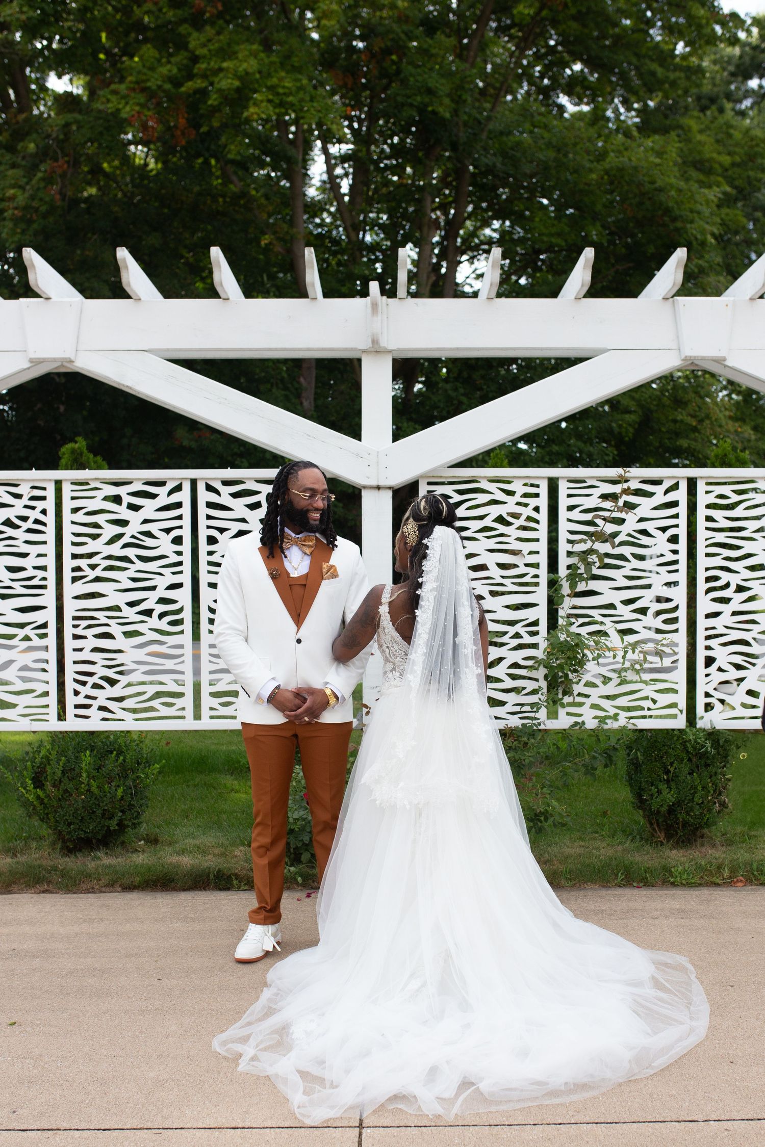 Couple poses under white pergola with decorative lattice panels.