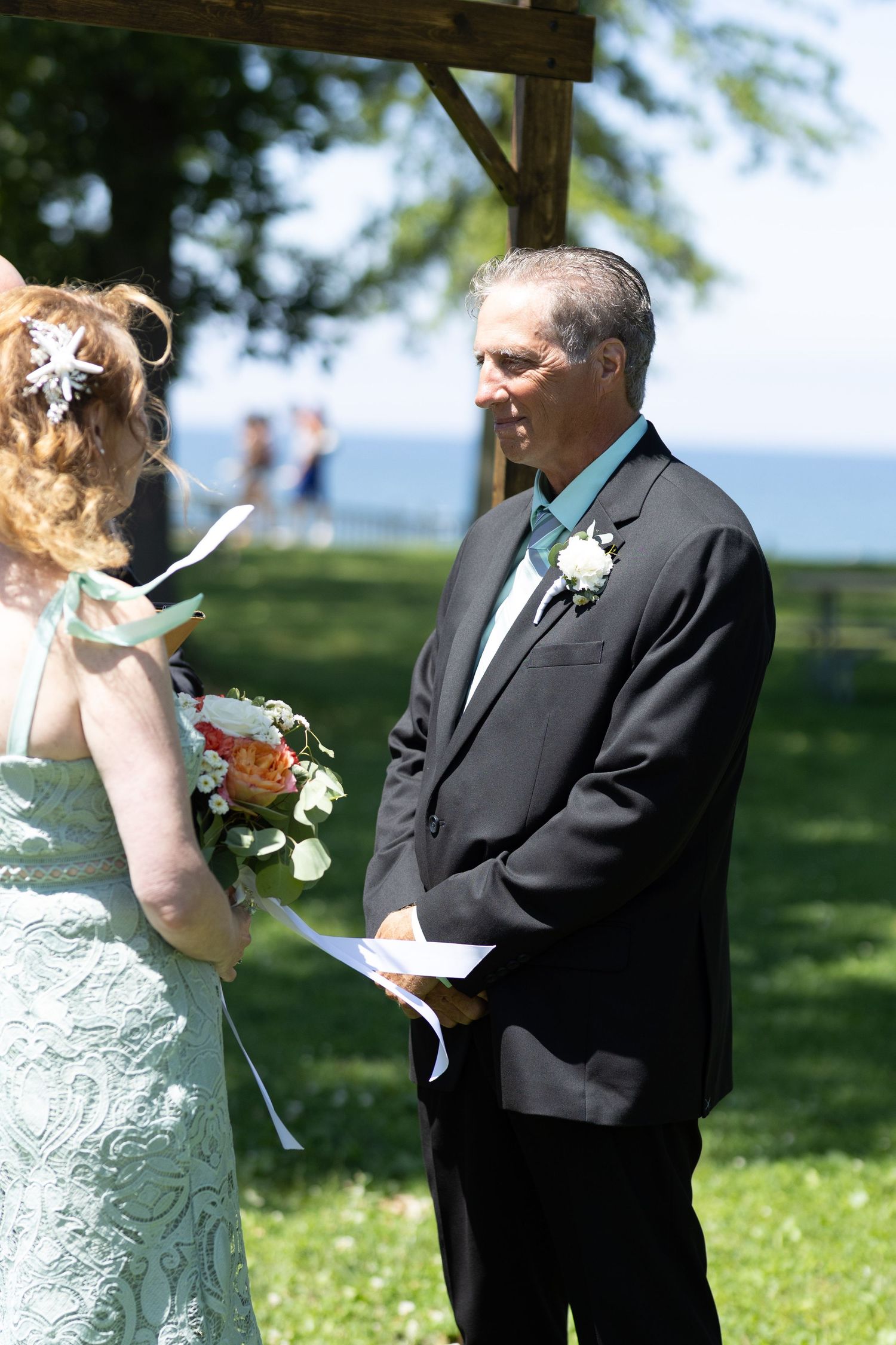 Wedding ceremony taking place in a sunny garden with a couple reading their vows.
