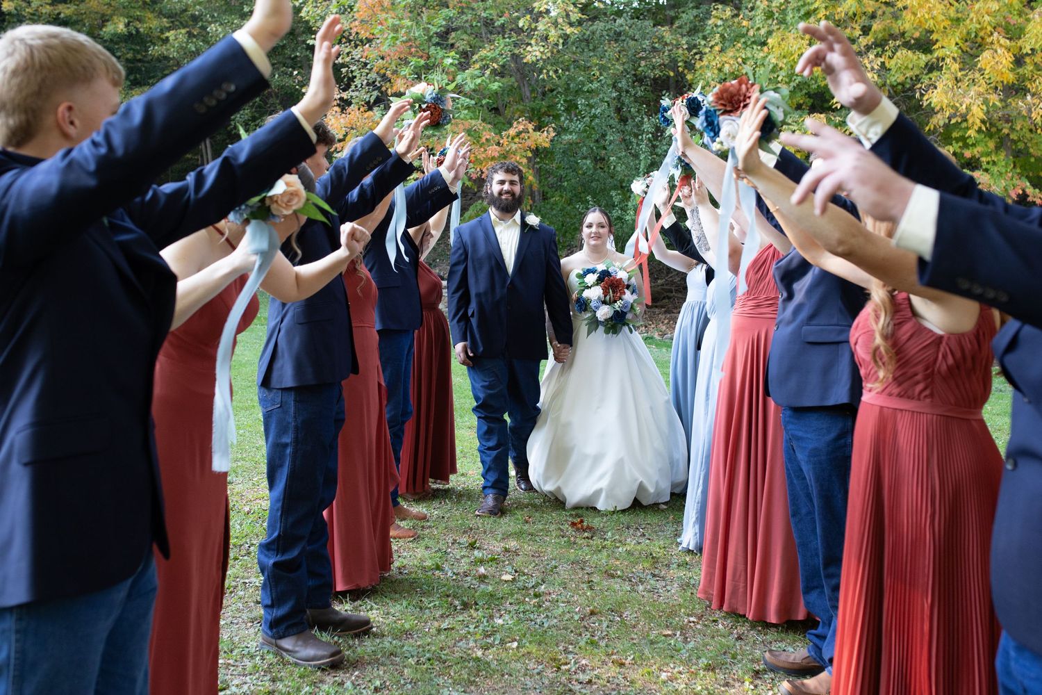 Wedding party forms celebratory tunnel with raised arms as couple walks through.