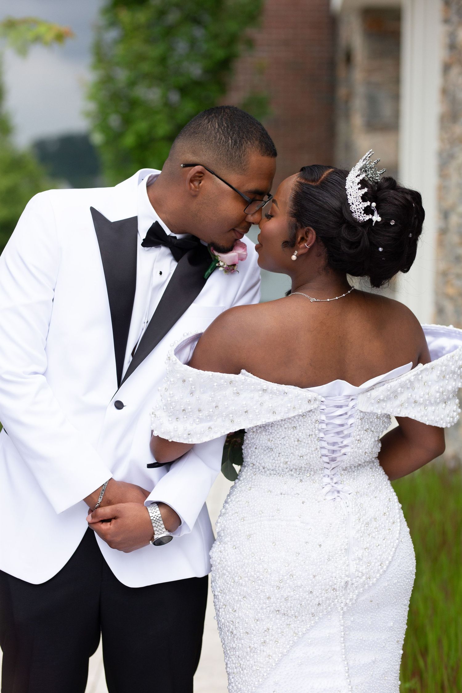 Elegant wedding portraits with white tuxedo and lace dress against outdoor backdrop.