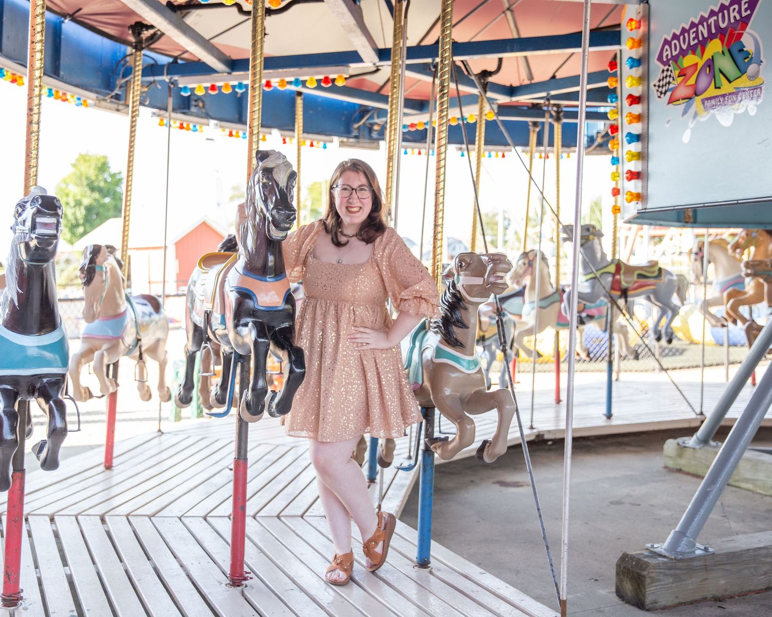 A carousel with decorated horses provides a whimsical backdrop for a photo at an amusement park.