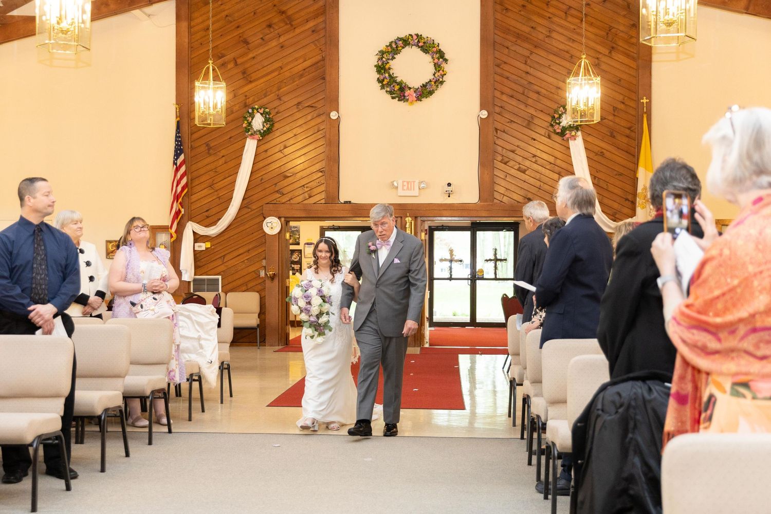Bride walking down the aisle with her father in a decorated church during a wedding ceremony.