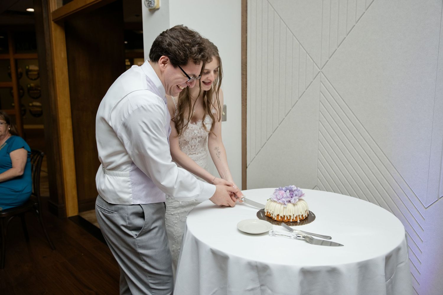 Bride and groom cutting their wedding cake together at a round table with white linen.