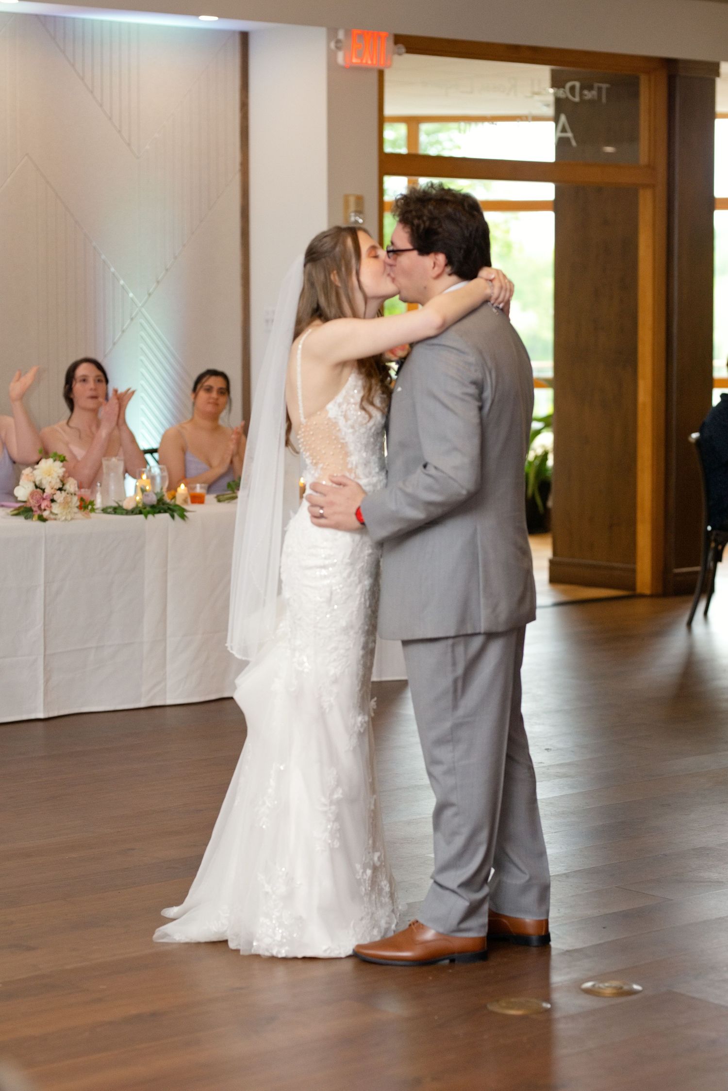 Bride and groom share a romantic kiss on the dance floor during wedding reception, bride in lace gown with veil.