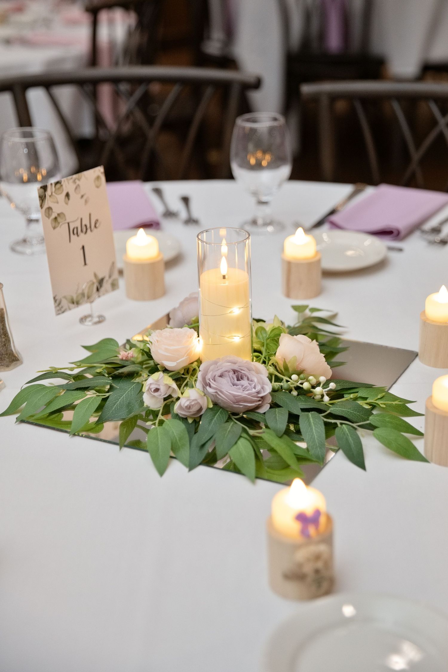Elegant wedding table centerpiece with candles, greenery, and lavender roses beside a Table 1 card.