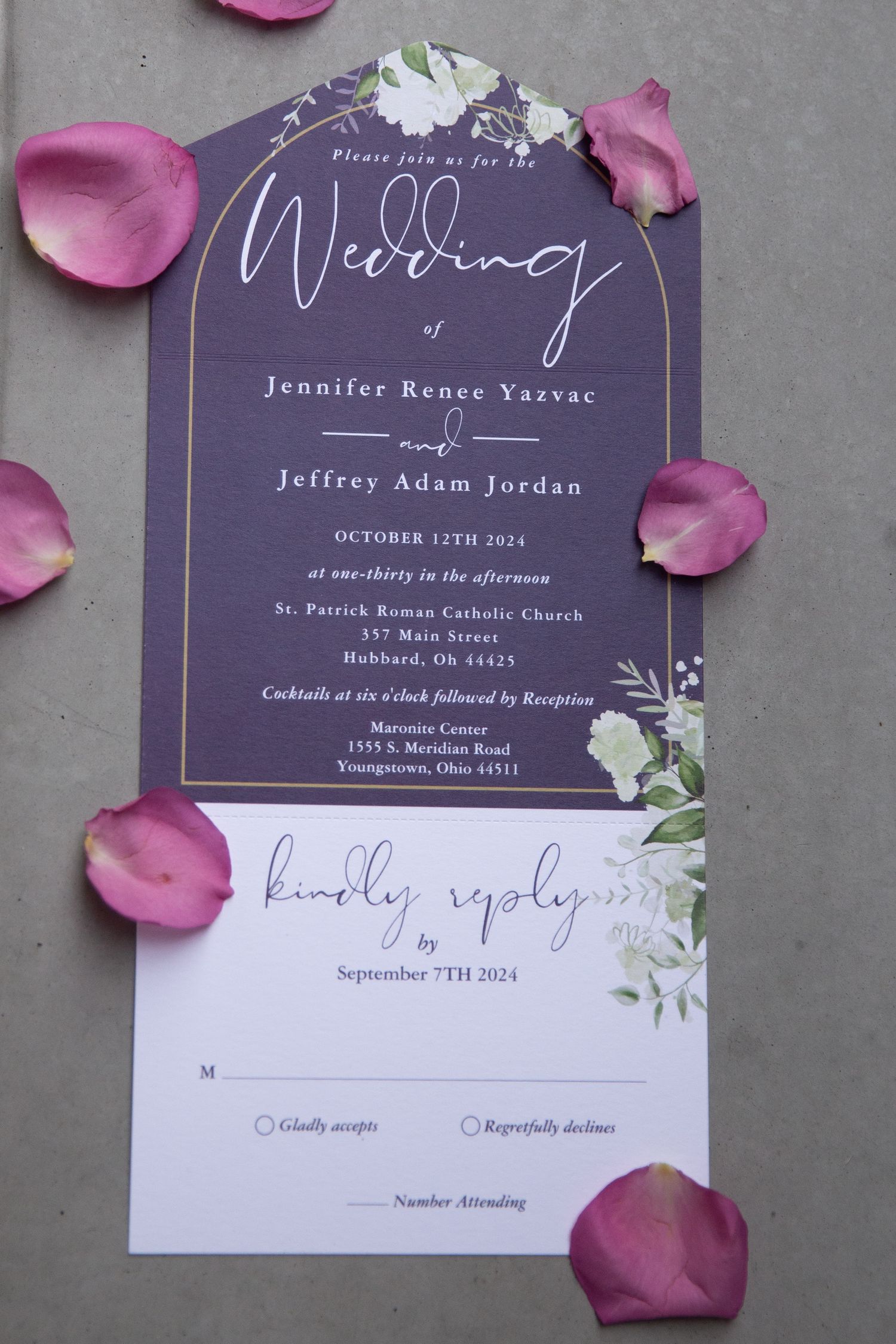 Purple wedding invitations with floral design and rose petals on gray background.