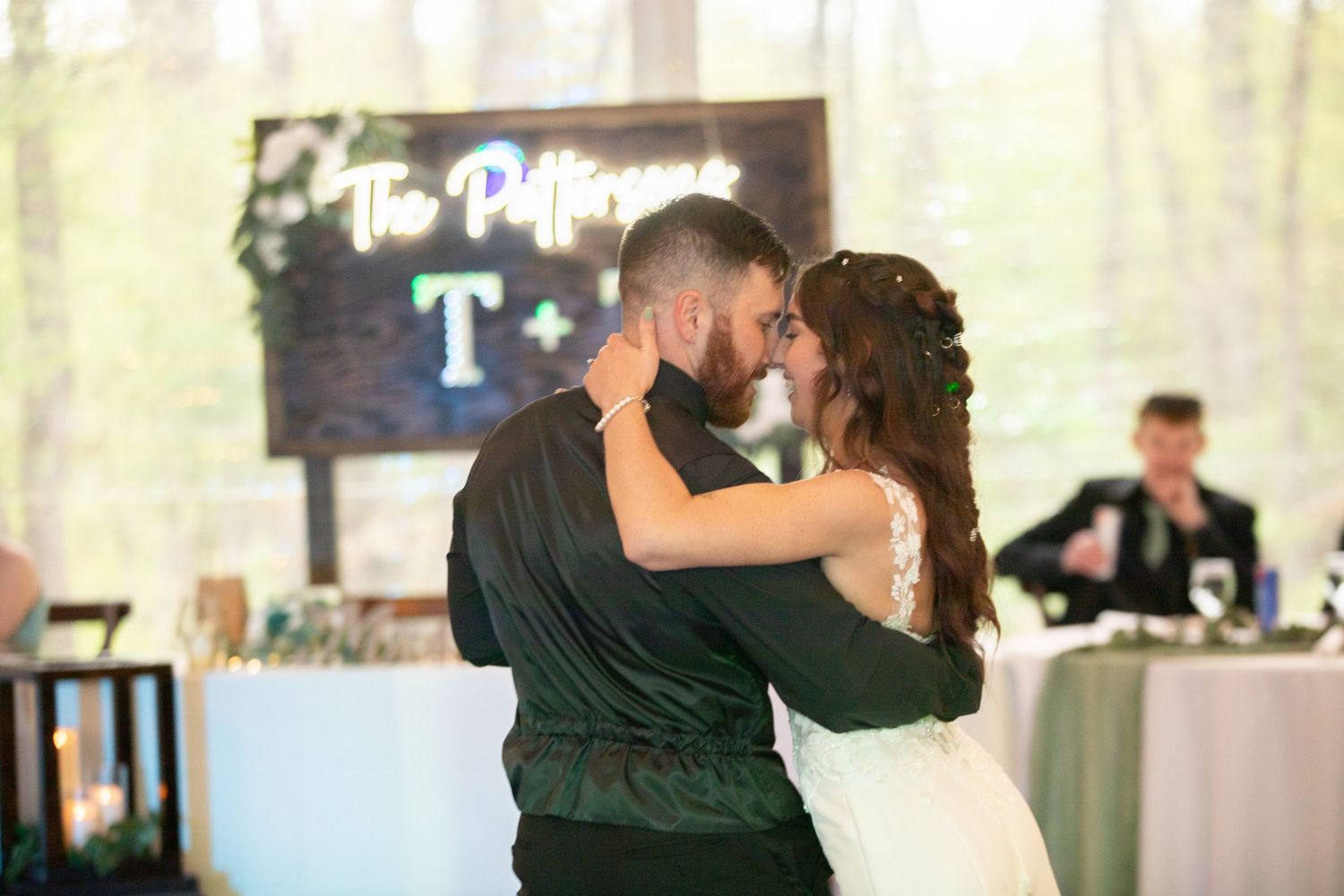 Bride and groom share their first dance at an elegant woodland wedding reception with neon sign backdrop.