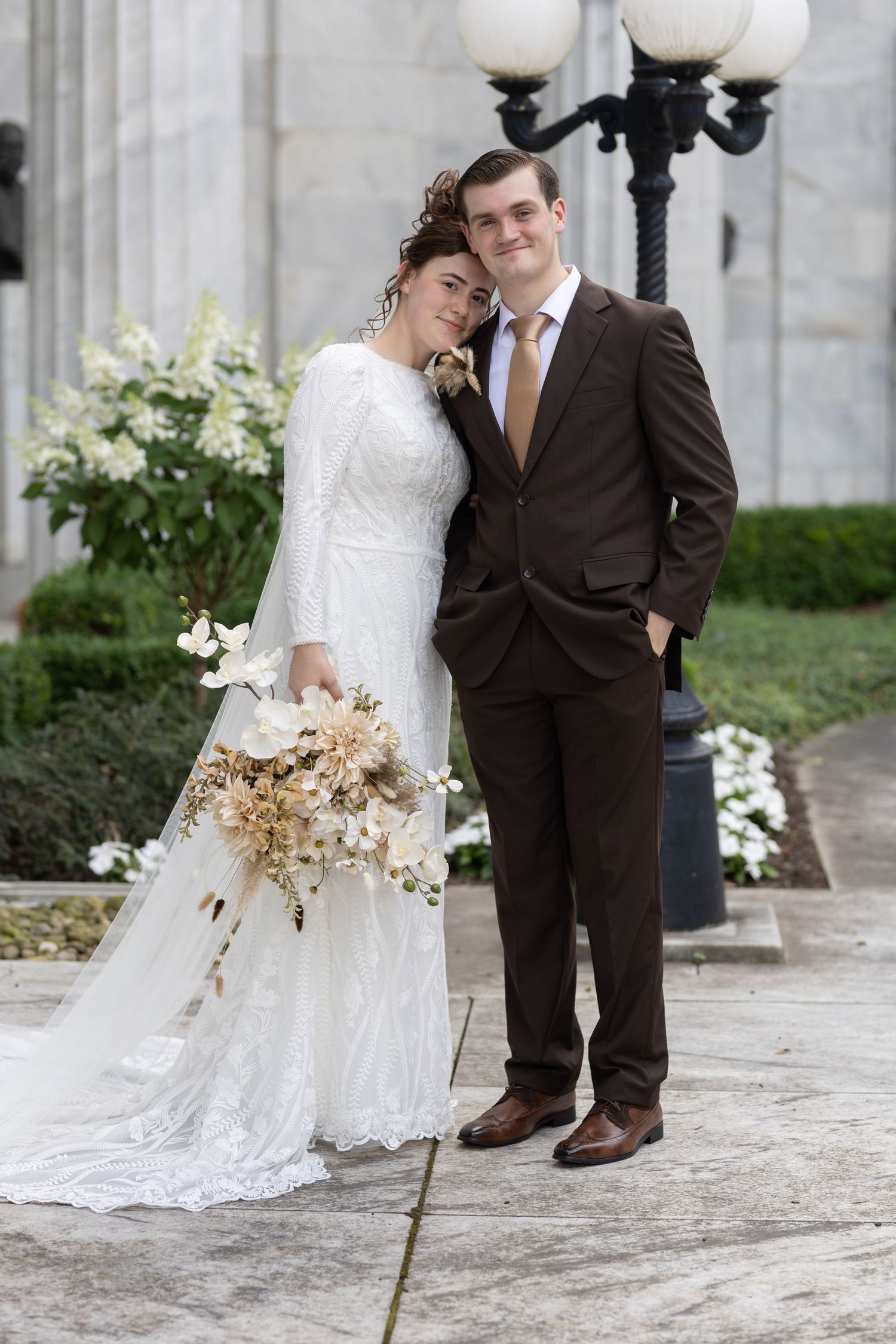 Wedding couple poses by ornate lamp post with dried floral bouquet.