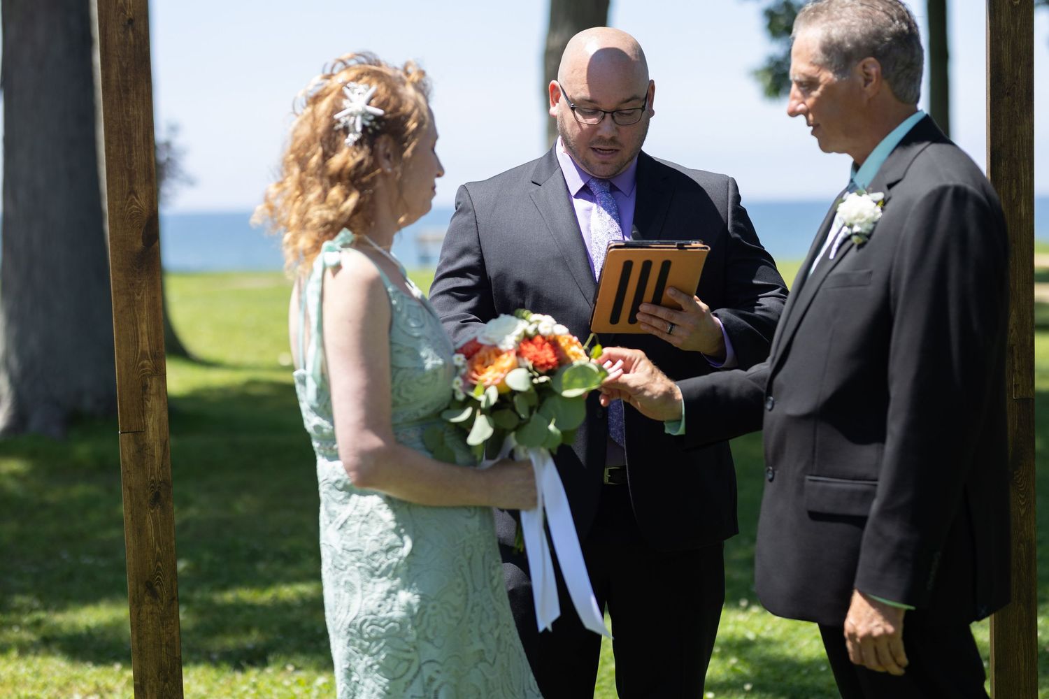 Wedding ceremony participants reading from papers during an outdoor celebration.