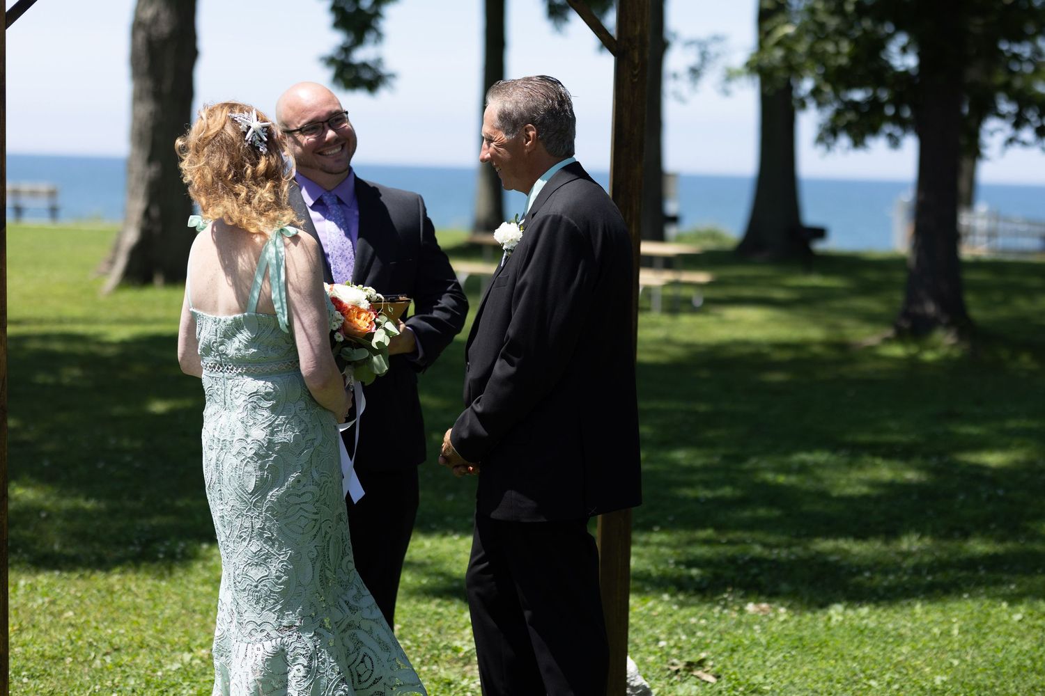 Outdoor wedding ceremony taking place on a grassy lawn with water view.
