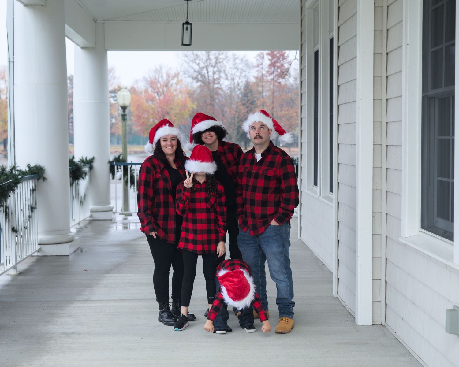 Family members in matching red and black buffalo check shirts gather on a columned white porch.