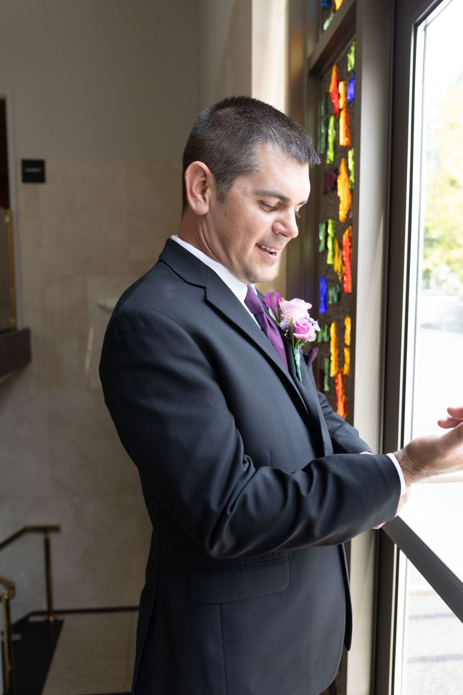 Man in black suit looking out window with colorful decorations.