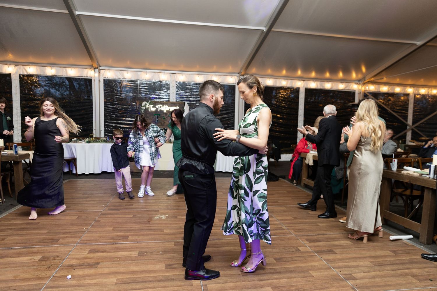 Couples dancing at an elegant outdoor wedding reception under string lights in a decorated tent venue.