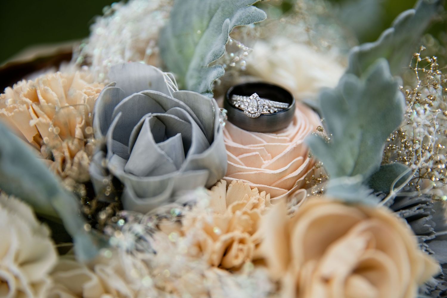 Diamond engagement ring nestled among gray and blush sola wood flowers in a bridal bouquet.