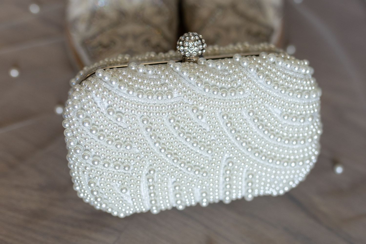 Elegant pearl-encrusted bridal clutch purse displayed on wooden surface.